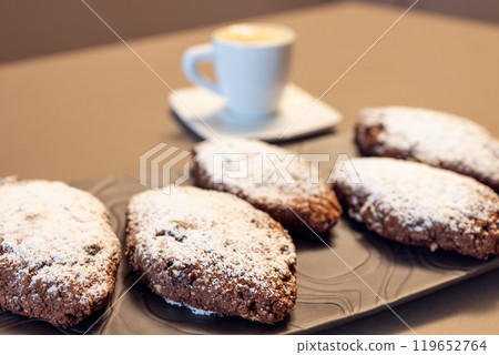 Pane dei Morti cookies topped with powdered sugar on dark plate with blurred espresso behind Pane dei Morti cookies topped with powdered sugar on dark plate with blurred espresso behind 119652764