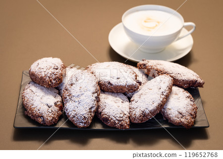 Italian Pane dei Morti cookies on dark plate with powdered sugar frothy cappuccino in background Italian Pane dei Morti cookies on dark plate with powdered sugar frothy cappuccino in background 119652768