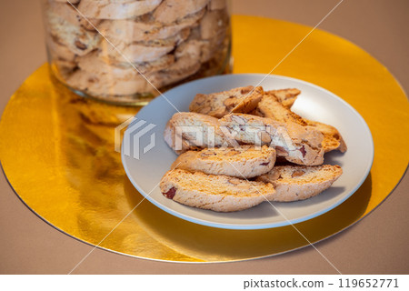 Plate of almond cantucci on reflective gold surface with jar vibrant crunchy nutty flavor 119652771