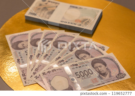 Japanese 5000 yen bills fanned on golden surface with stack behind showing wealth tradition Japanese 5000 yen bills fanned on golden surface with stack behind showing wealth tradition 119652777