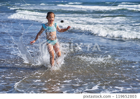 An 8 year old girl in a swimsuit having fun in the sea waves. 119652803
