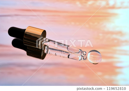 A pipette with facial serum against a sunset background in bright orange tones. 119652810