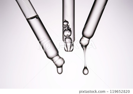 Three pipettes with a cosmetic product. Serum or fluid drips from one of them. Three pipettes with a cosmetic product. Serum or fluid drips from one of them. 119652820