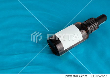 Amber glass dropper bottle with a blank label floating on a blue water surface ideal for branding mockups 119652844