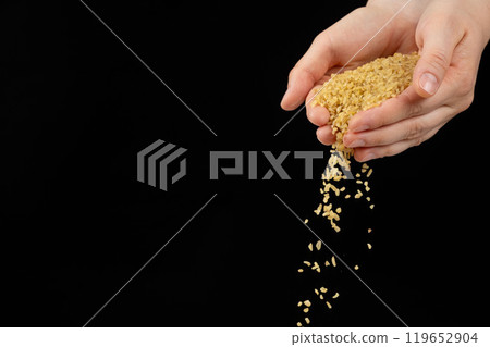 Hands pouring raw uncooked bulgur cereals on a black background space for text Hands pouring raw uncooked bulgur cereals on a black background space for text 119652904