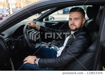 Success in motion. Handsome young man in leather jacket while sitting in a car 119653344