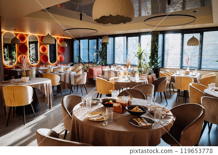 Modern restaurant interior with elegant decor, tables, and lighting creating warm dining ambiance 119653778