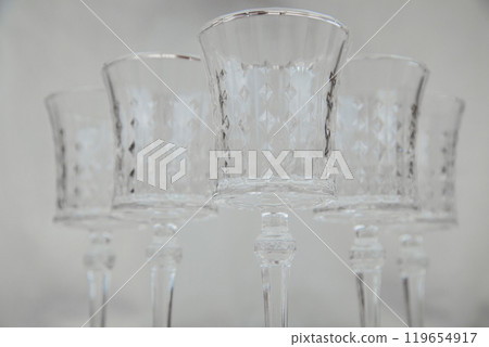 Crystal wine glasses with expanded edges and faceted pattern stand in a wedge on a white background, the first glass in focus, the others are in focus on both sides of him, bottom view. High quality Crystal wine glasses with expanded edges and faceted pattern stand in a wedge on a white background, the first glass in focus, the others are in focus on both sides of him, bottom view. High quality 119654917