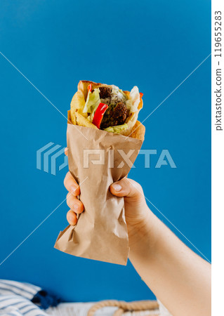 Hand holding falafel wrap with vegetables and tahini sauce, takeaway or street food lovers 119655283