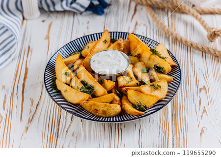 Golden potato wedges with herbs and creamy dip, perfect for any meal or snack 119655290