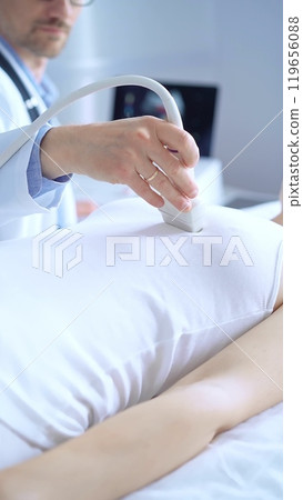 Doctor man wearing white protective gloves is using ultrasound equipment on the breast of a female patient. Mammary gland health 119656088