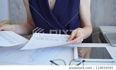 Businesswoman with dark blue dress is reviewing financial reports and pointing at a chart with a pen. Business concept Businesswoman with dark blue dress is reviewing financial reports and pointing at a chart with a pen. Business concept 119656095