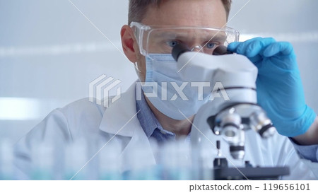 Man scientist with protective glasses, mask and gloves is using microscope in laboratory, portrait of researcher. Microbiology science concept 119656101