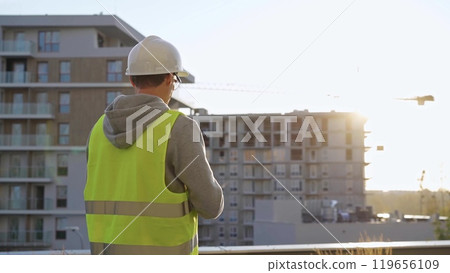 Man constructive engineer with white hard hat and safety vest is using a tablet computer while inspecting a construction site at sunrise in early morning Man constructive engineer with white hard hat and safety vest is using a tablet computer while inspecting a construction site at sunrise in early morning 119656109
