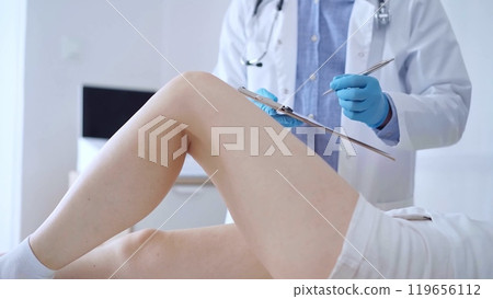 Doctor man wearing blue medical gloves examines a patient's knee 119656112