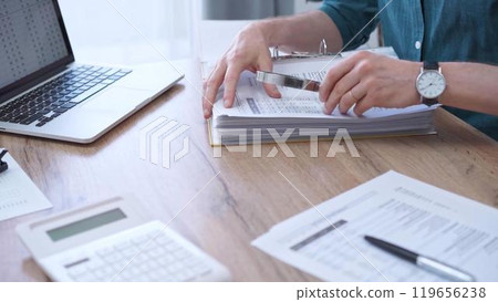 Businessman or auditor wearing green shirt is reviewing financial documents with magnifying glass. Business work process in bookkeeping office. Taxes Businessman or auditor wearing green shirt is reviewing financial documents with magnifying glass. Business work process in bookkeeping office. Taxes 119656238