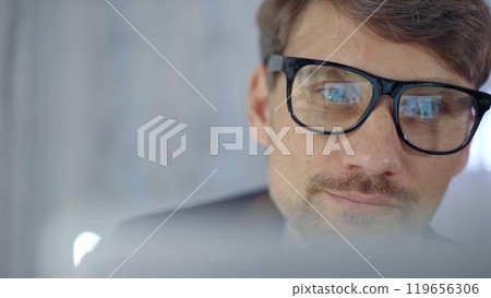 Businessman with glasses looking intently obscured partially by a translucent surface of laptop. Business concept Businessman with glasses looking intently obscured partially by a translucent surface of laptop. Business concept 119656306