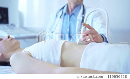 Doctor man wearing a white coat using an ultrasound machine on a female patient examining internal organs. Preventive therapy in medicine Doctor man wearing a white coat using an ultrasound machine on a female patient examining internal organs. Preventive therapy in medicine 119656318