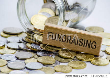 Fundraising text on wooden block with coins and jar background. Charity concept 119659003