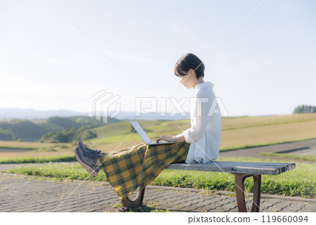 A young woman sitting on a bench and using a laptop A young woman sitting on a bench and using a laptop 119660094