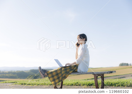 A young woman sitting on a bench and using a laptop 119660102