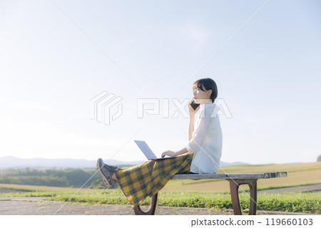 A young woman sitting on a bench and using a laptop 119660103