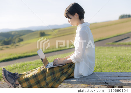 A young woman sitting on a bench and using a laptop A young woman sitting on a bench and using a laptop 119660104