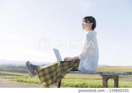 坐在長椅上使用電腦的年輕女子 坐在長椅上使用電腦的年輕女子 119660105