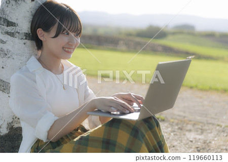 A young woman sitting on a bench and using a laptop 119660113