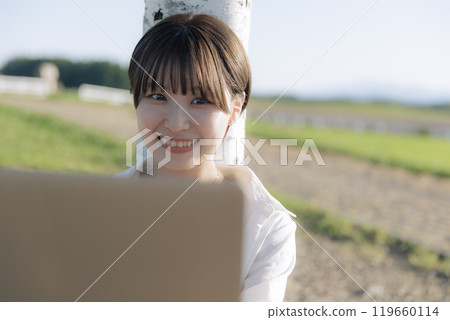 A young woman sitting on a bench and using a laptop 119660114