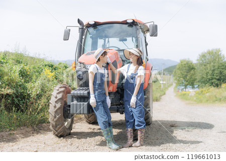 Two young women standing in front of a tractor 119661013