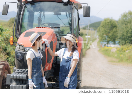 Two young women standing in front of a tractor 119661018