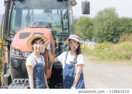 Two young women standing in front of a tractor 119661019