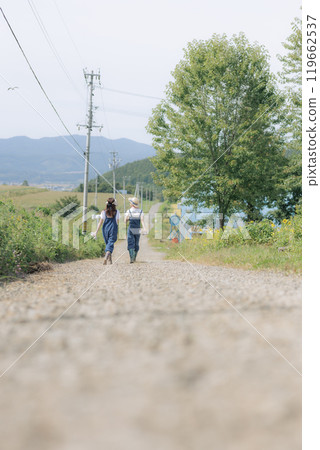 Young women walking along a farm road 119662537