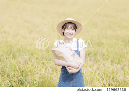 A young woman standing in front of a rice field holding newly harvested rice 119662886