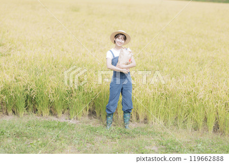 A young woman standing in front of a rice field holding newly harvested rice A young woman standing in front of a rice field holding newly harvested rice 119662888
