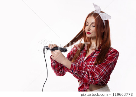A Woman is Styling Her Hair with a Straightener While Wearing a Fashionable and Trendy Outfit A Woman is Styling Her Hair with a Straightener While Wearing a Fashionable and Trendy Outfit 119663778