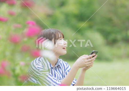 A young woman sitting and playing with her smartphone 119664015
