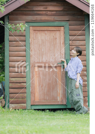 Young woman standing in front of a log house 119664168