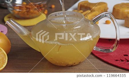 Sea buckthorn, orange and spice tea in teapot in kitchen. Healthy eating and seasons.  119664335