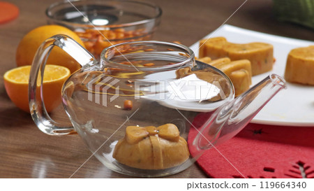 Sea buckthorn, orange and spice tea from frozen briquette in teapot in kitchen. Healthy eating and seasons. Quick batch of beverages. 119664340