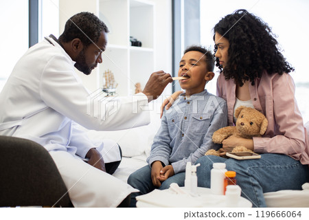 Doctor examining sick boy's throat with mother by his side 119666064