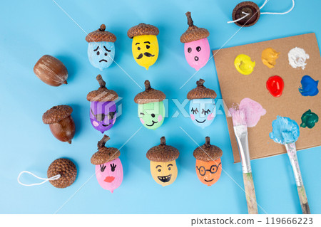 Emoji faces acorns in colorful paint on blue background. Flat lay autumn craft idea, ideal for greeting cards, posters, banners, and creative DIY projects. Fun and festive mood 119666223