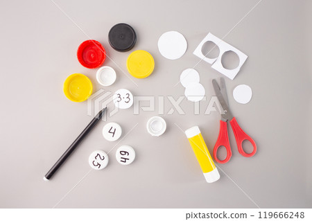 plastic bottle caps with hand-written numbers and multiplication facts on a gray background. glue, scissors and marker, step in creative DIY process, Educational math activity for kids, 119666248