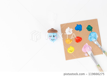 Colorful hand painted acorn next to a paint palette and brushes on a white background. Studio shot for craft projects and autumn decorations. DIY and creativity concept. Colorful hand painted acorn next to a paint palette and brushes on a white background. Studio shot for craft projects and autumn decorations. DIY and creativity concept. 119666275