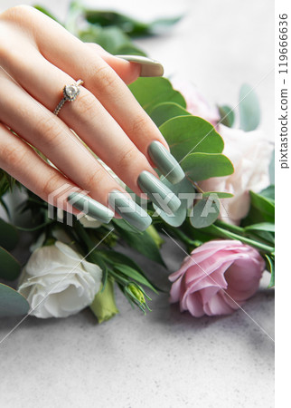 Elegant hand adorned with a ring showcasing stylish green nails beside a bouquet  119666636