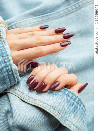 A close-up of elegantly manicured hands showcasing deep burgundy nail polish  119666641