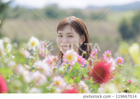 A young woman looking at the camera from behind the cosmos field 119667014