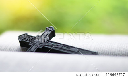 Dark brown wooden cross on an old open book symbolizing the spread of Jesus Christs love among Christians reflecting faith devotion and the importance of Christian teachings. 119668727