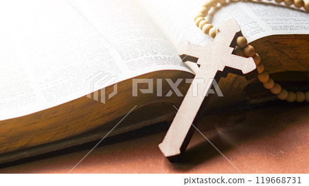Brown wooden cross on an old open book symbolizing the spread of Jesus Christs love among Christians reflecting faith devotion and the importance of Christian teachings. 119668731